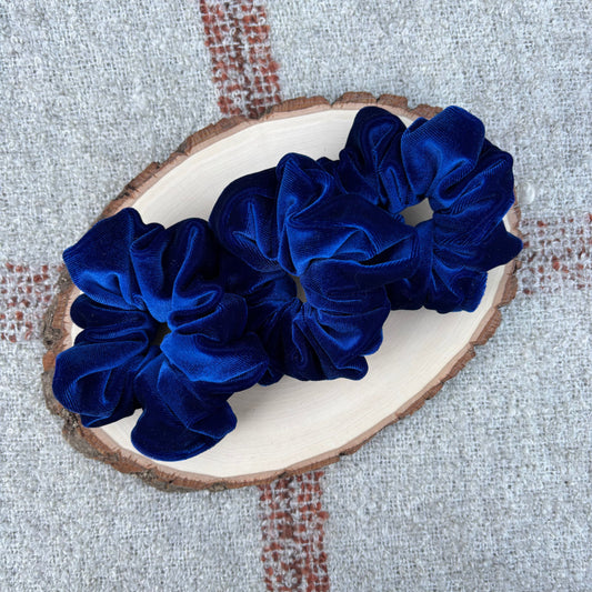 Three blue scrunchies on a wooden slice with a textured background